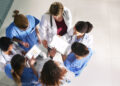 A group of doctors looking at a tablet Description automatically generated with low confidence
