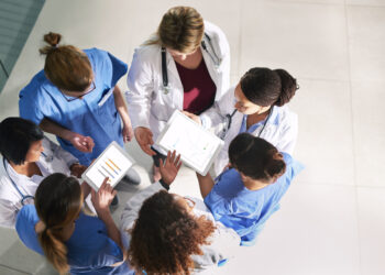A group of doctors looking at a tablet Description automatically generated with low confidence