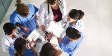 A group of doctors looking at a tablet Description automatically generated with low confidence